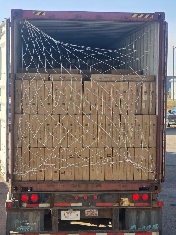 The same cartons behind a cargo net in an open container on a trailer with an Alberta plate