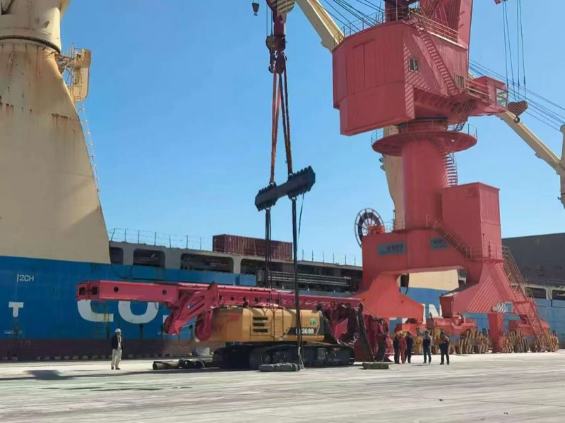 A port crane lifting a flat-rack load aboard.