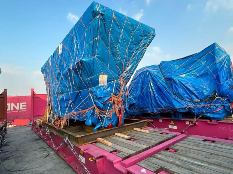 Machinery covered with tarpaulins and lashed on a flat-rack.